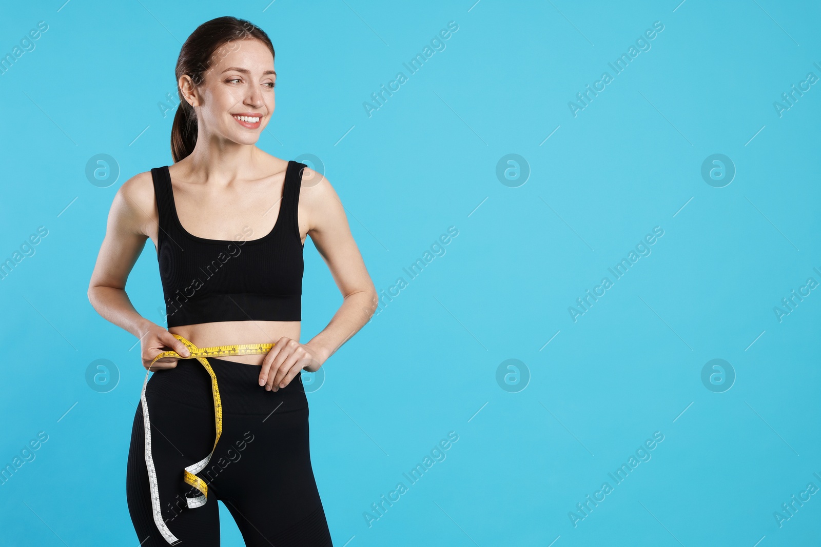 Photo of Beautiful woman measuring her belly with tape on light blue background, space for text