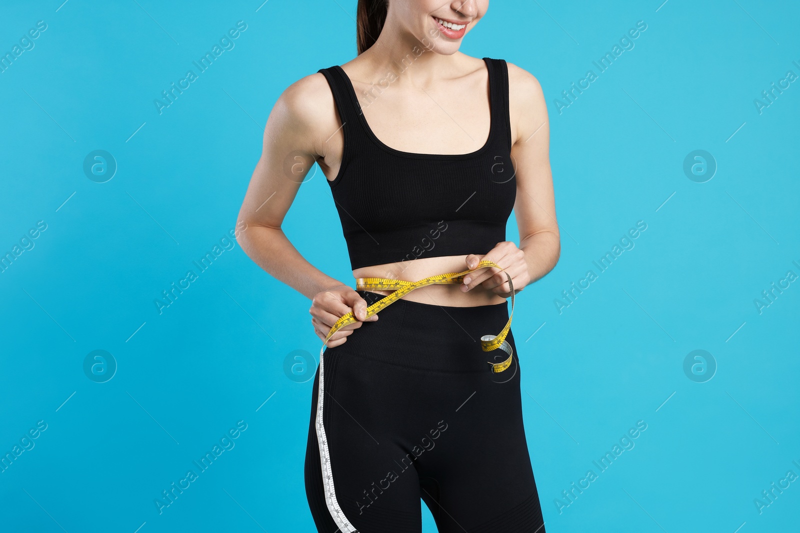 Photo of Woman measuring her belly with tape on light blue background, closeup