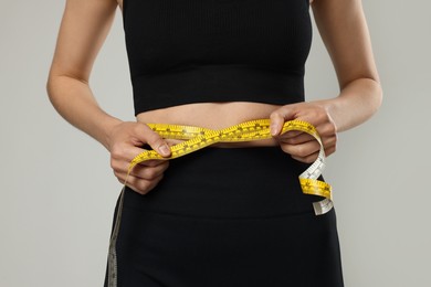 Photo of Woman measuring her belly with tape on gray background, closeup