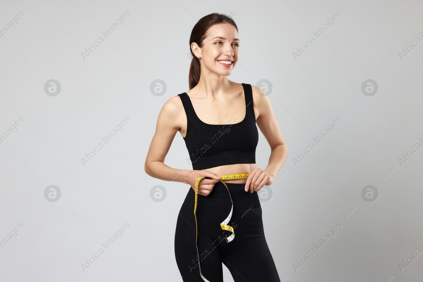 Photo of Beautiful woman measuring her belly with tape on gray background