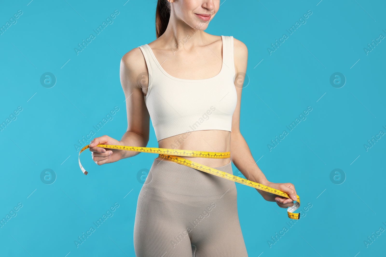 Photo of Beautiful woman measuring her belly with tape on light blue background, closeup