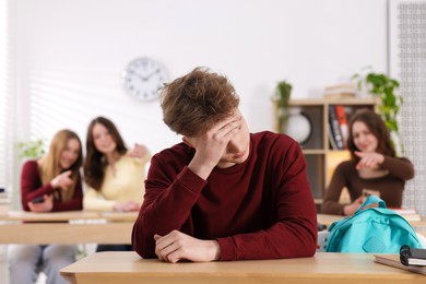 Photo of Bullying. Upset teenage boy and schoolmates pointing at him in classroom, selective focus