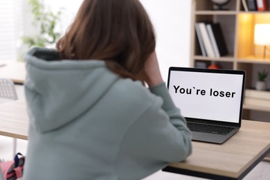 Photo of Cyber bullying. Upset teenage girl and laptop with text You Loser at desk indoors