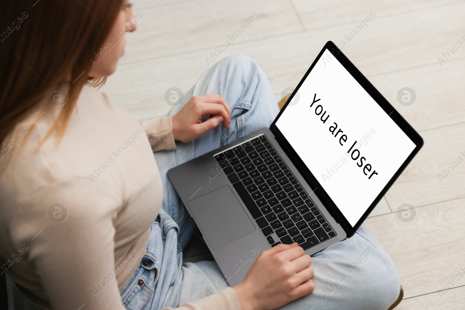Cyber bullying. Upset teenage girl looking at laptop with text You Loser on floor indoors, closeup Photo of Cyber bullying. Upset teenage girl looking at laptop with text You Loser on floor indoors, closeup