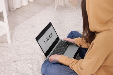 Photo of Cyber bullying. Upset teenage girl and laptop with text You Loser on floor indoors, closeup