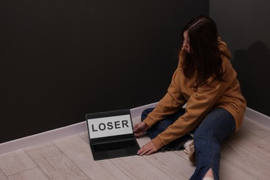 Photo of Cyber bullying. Upset teenage girl and laptop with text You Loser on floor indoors. Space for text