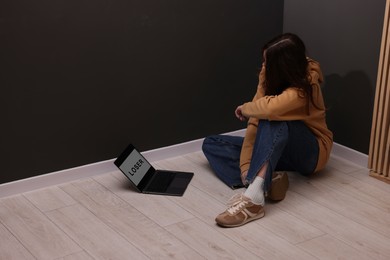 Photo of Cyber bullying. Upset teenage girl and laptop with text You Loser on floor indoors. Space for text