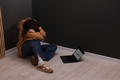 Photo of Cyber bullying. Upset teenage girl and laptop with text You Loser on floor indoors. Space for text