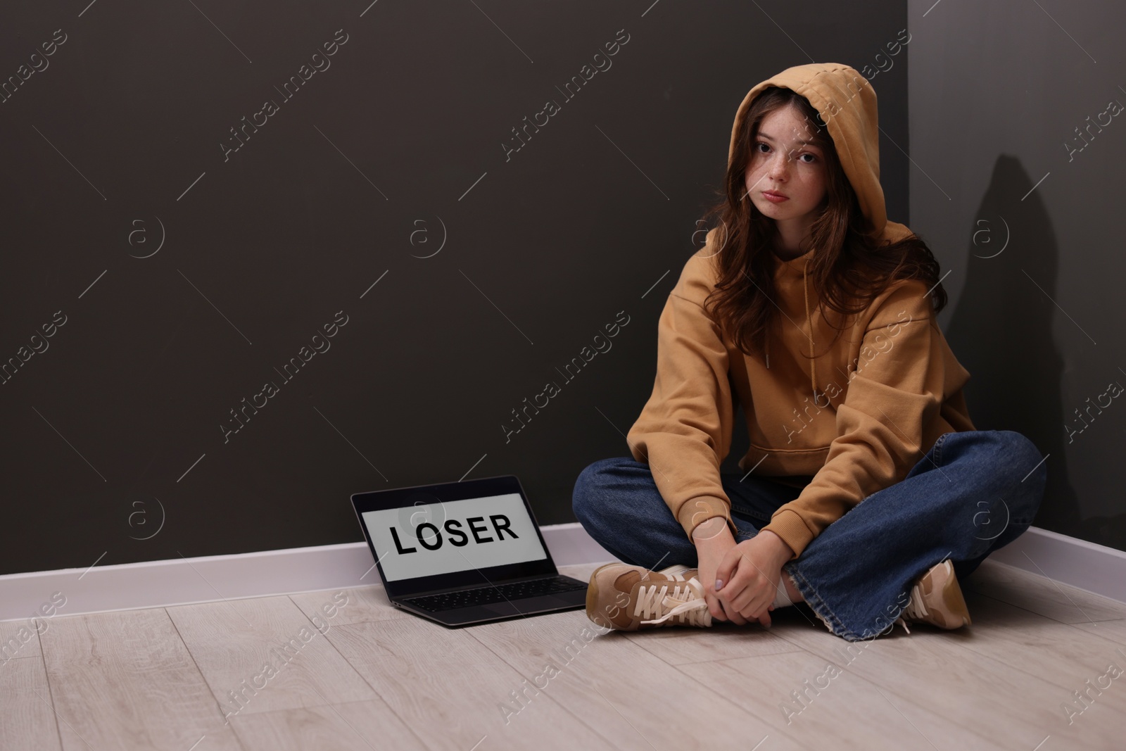 Cyber bullying. Upset teenage girl and laptop with text You Loser on floor indoors. Space for text Photo of Cyber bullying. Upset teenage girl and laptop with text You Loser on floor indoors. Space for text
