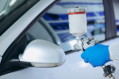Photo of Worker painting car in body shop, closeup