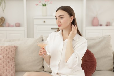 Photo of Beautiful woman with glass of alcoholic drink sitting on sofa at home