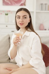 Photo of Beautiful woman with glass of alcoholic drink sitting on sofa at home