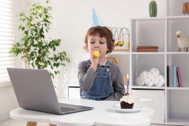 Photo of Little boy celebrating his birthday while having video call via laptop at table indoors