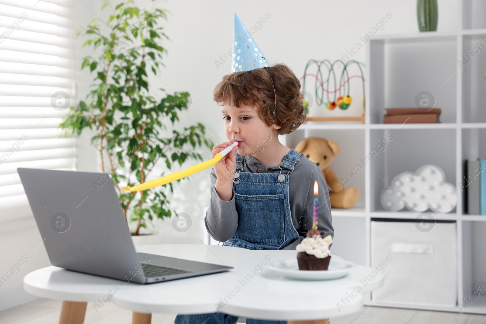Photo of Little boy celebrating his birthday while having video call via laptop at table indoors
