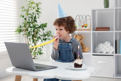 Photo of Little boy celebrating his birthday while having video call via laptop at table indoors