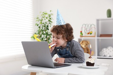 Photo of Little boy celebrating his birthday while having video call via laptop at table indoors