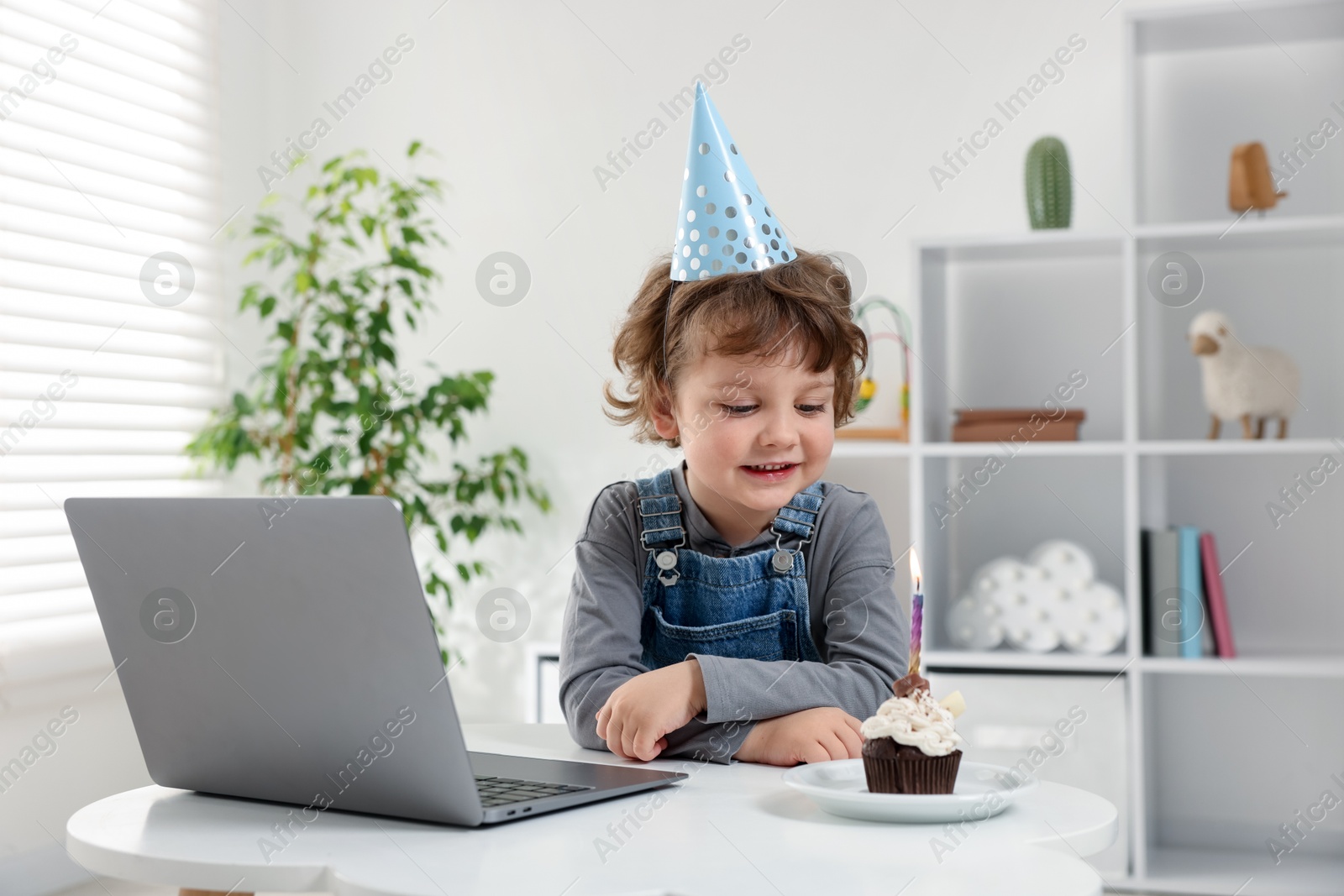 Photo of Birthday celebration. Little boy with cupcake having video call via laptop at table indoors