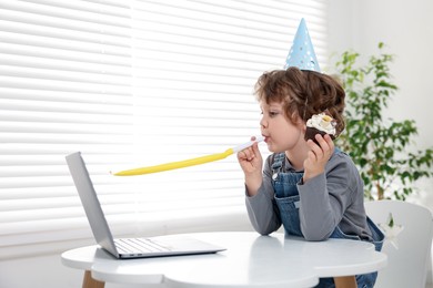 Photo of Little boy celebrating his birthday while having video call via laptop at table indoors. Space for text