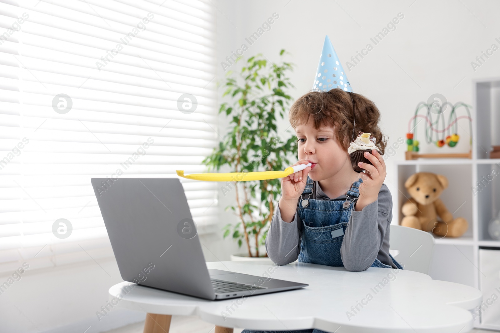 Photo of Little boy celebrating his birthday while having video call via laptop at table indoors. Space for text