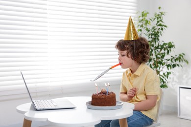 Photo of Little boy celebrating his birthday while having video call via laptop at table indoors. Space for text