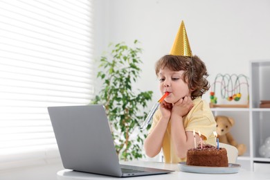 Photo of Little boy celebrating his birthday while having video call via laptop at table indoors. Space for text