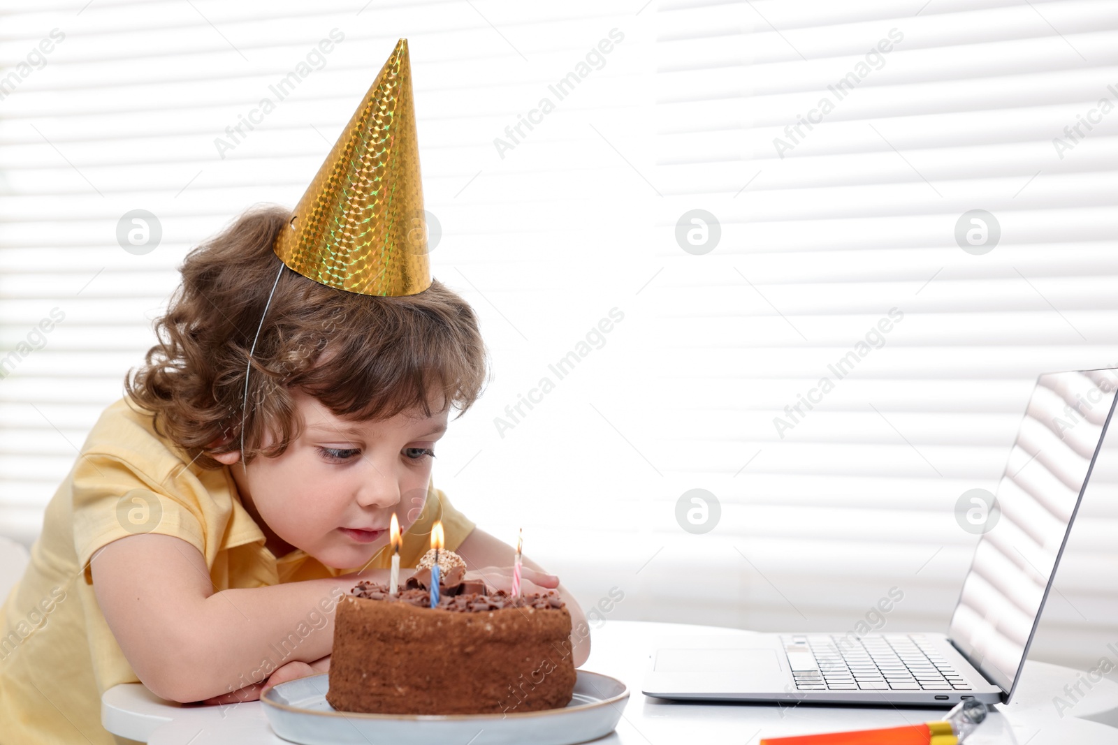 Photo of Birthday celebration. Little boy with cake having video call via laptop at table indoors. Space for text