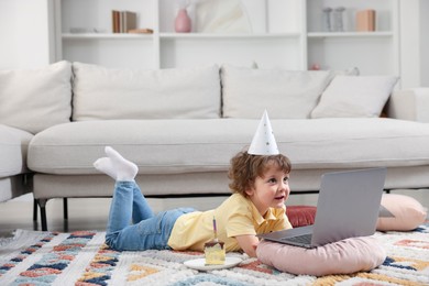 Photo of Birthday celebration. Little boy with piece of cake having video call via laptop at home. Space for text