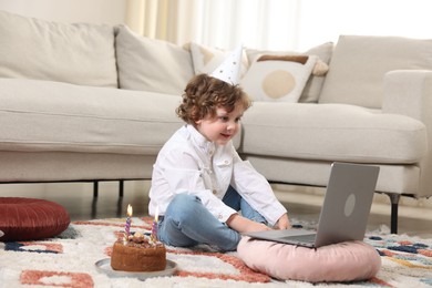 Photo of Birthday celebration. Little boy with cake having video call via laptop at home