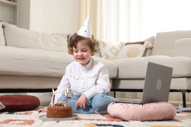 Photo of Birthday celebration. Little boy with cake having video call via laptop at home