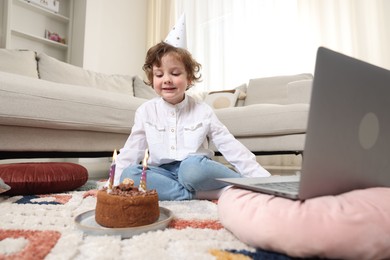 Photo of Birthday celebration. Little boy with cake having video call via laptop at home