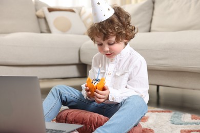 Photo of Birthday celebration. Little boy with cupcake having video call via laptop at home
