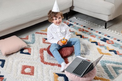 Photo of Birthday celebration. Little boy with cupcake having video call via laptop at home