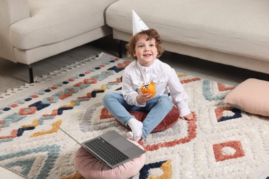 Photo of Birthday celebration. Little boy with cupcake having video call via laptop at home