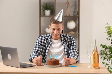 Photo of Birthday celebration. Man with cake and sparkling wine having video call via laptop at desk indoors