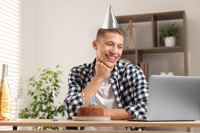 Photo of Birthday celebration. Man with cake having video call via laptop at desk indoors