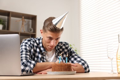 Photo of Birthday celebration. Man with cake having video call via laptop at desk indoors