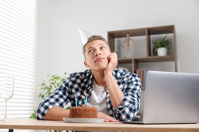 Photo of Birthday celebration. Man with cake having video call via laptop at desk indoors