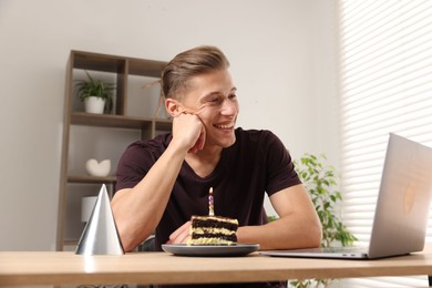 Photo of Birthday celebration. Man with cake having video call via laptop at table indoors, low angle view