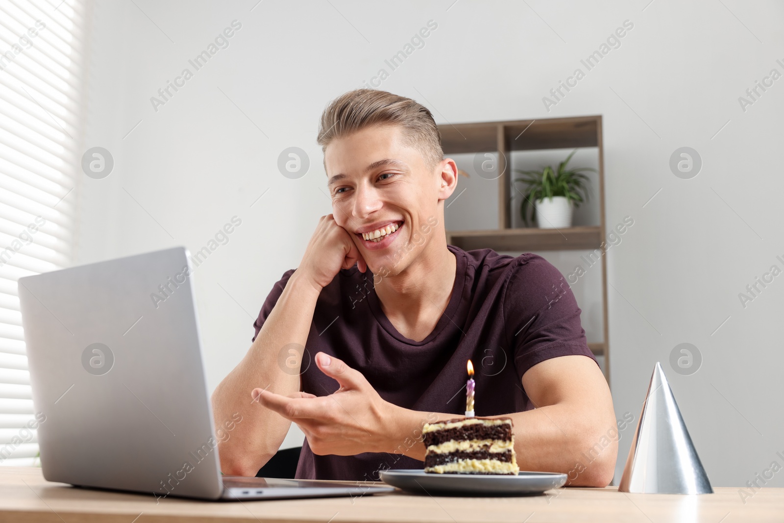 Photo of Birthday celebration. Man with cake having video call via laptop at table indoors, low angle view