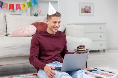 Photo of Man with piece of cake celebrating his birthday and having video call via laptop at home
