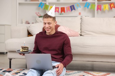 Photo of Man with piece of cake celebrating his birthday and having video call via laptop at home