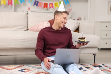Photo of Man with piece of cake celebrating his birthday and having video call via laptop at home