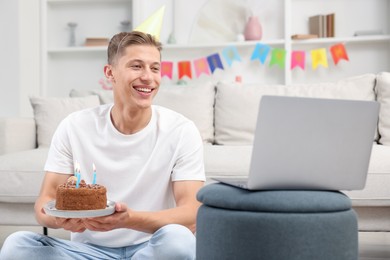 Photo of Man with cake celebrating his birthday and having video call via laptop at home