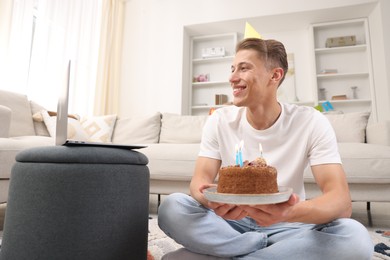 Photo of Man with cake celebrating his birthday and having video call via laptop at home