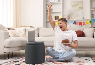 Photo of Man with cake celebrating his birthday and having video call via laptop at home