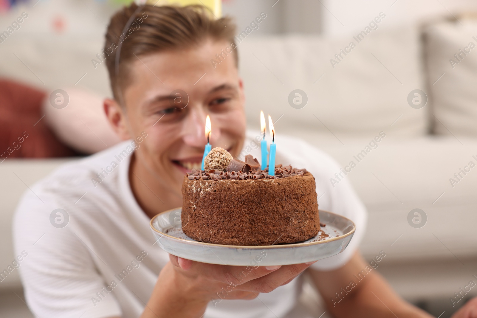 Photo of Birthday celebration. Happy man holding cake with burning candles indoors, selective focus