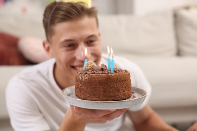 Photo of Birthday celebration. Happy man holding cake with burning candles indoors, selective focus