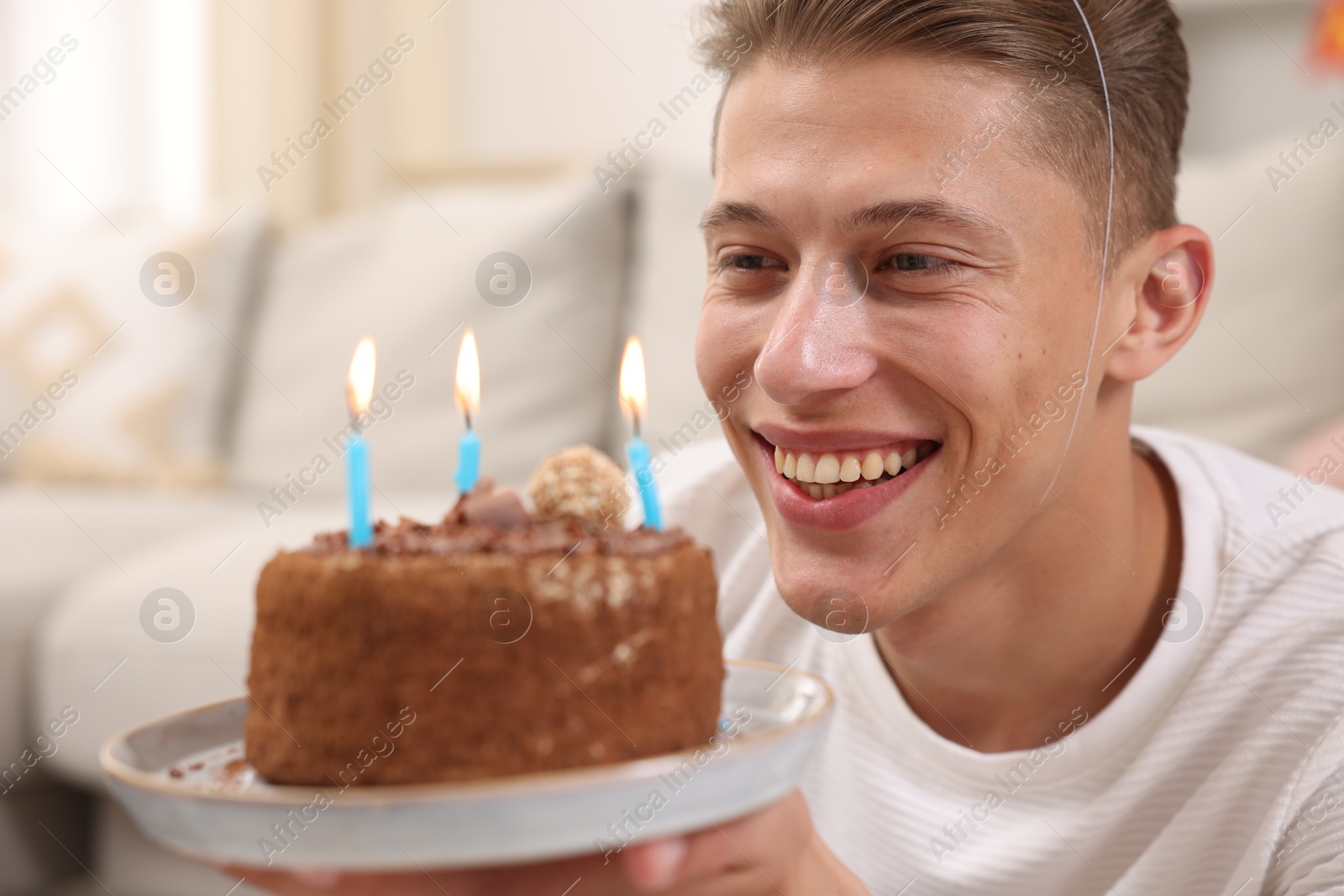Photo of Birthday celebration. Happy man holding cake with burning candles indoors, selective focus