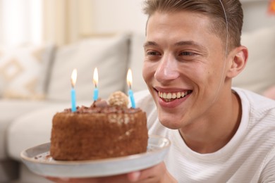 Photo of Birthday celebration. Happy man holding cake with burning candles indoors, selective focus