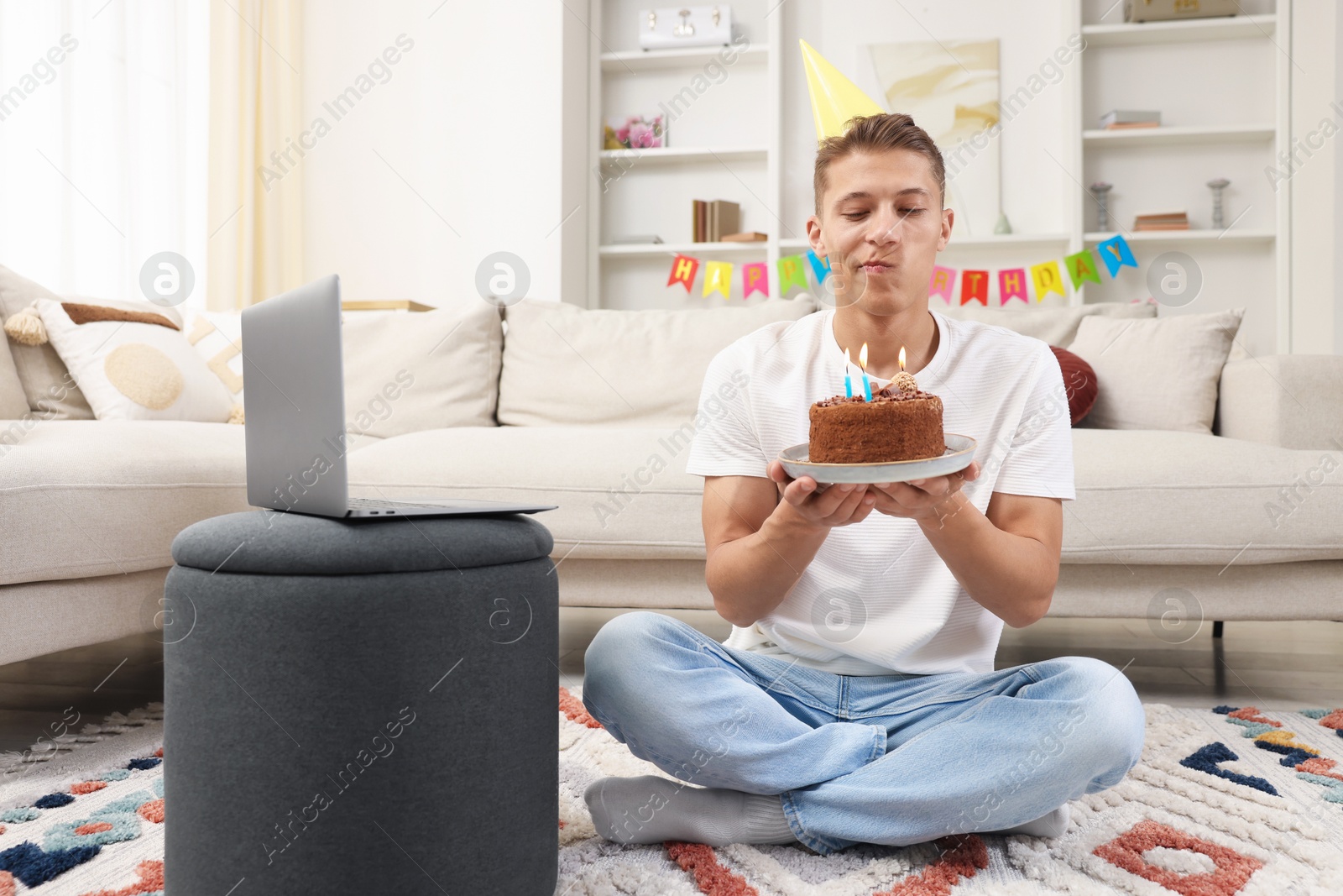 Photo of Birthday celebration. Man with cake making wish while having video call via laptop at home